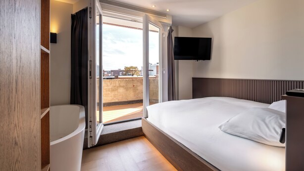 Une chambre d’hôtel avec un lit, un téléviseur fixé au mur et une porte coulissante donnant sur un balcon.