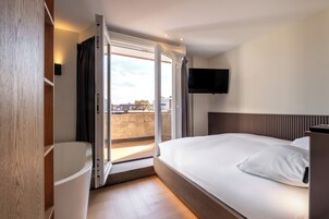 Quarto de hotel com uma cama, televisão fixada na parede e porta de correr para uma varanda.