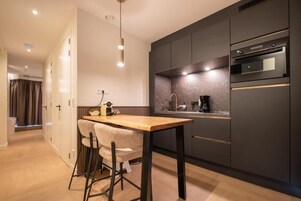 Uma cozinha moderna com armários escuros, uma mesa de madeira e um forno embutido.