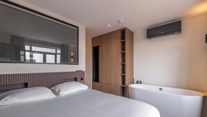 Une chambre moderne avec un grand lit, une armoire intégrée, un téléviseur fixé au mur et une baignoire sur pied.