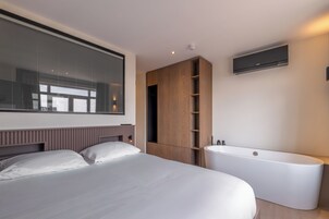 Un dormitorio moderno con una cama grande, un armario empotrado, un televisor montado en la pared y una bañera independiente.