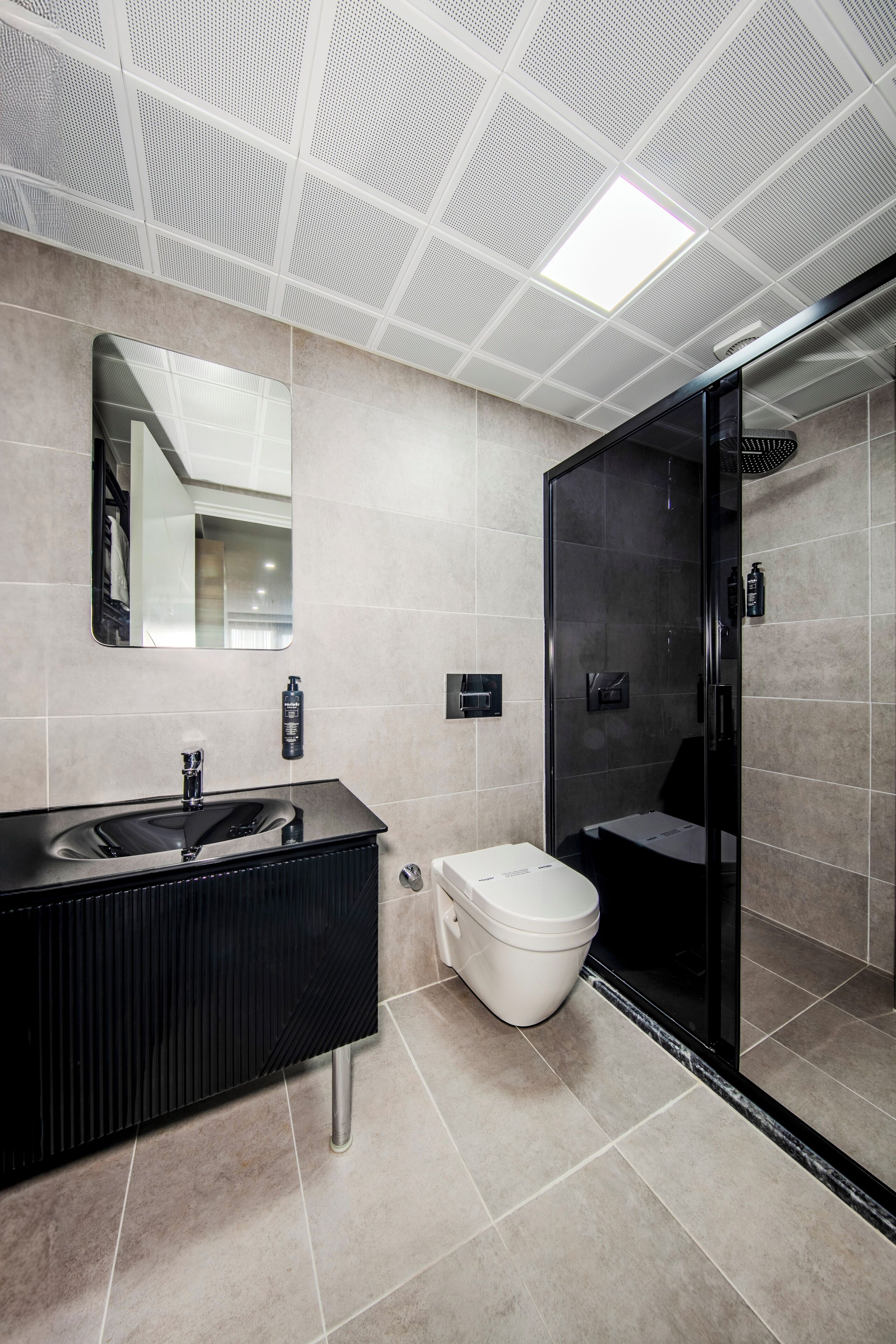 Une salle de bain moderne avec un meuble-lavabo noir, des toilettes blanches et une douche à parois de verre.
