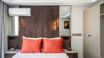 Una habitación de hotel con cama, dos mesitas de noche, aire acondicionado, espejo, luz en la pared y una puerta con manija.