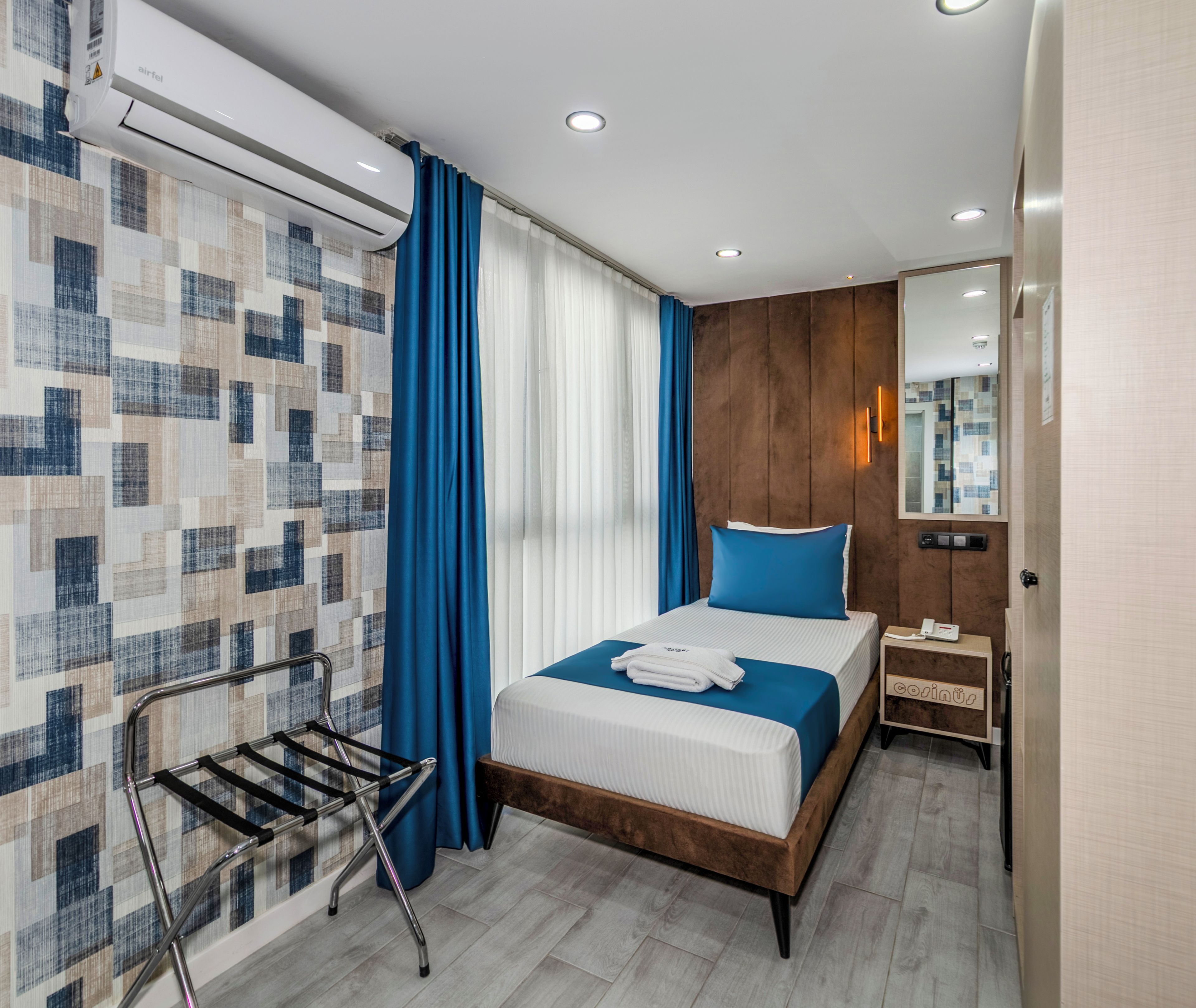 Ett modernt hotellrum med en säng, ett sängbord, en spegel och en väggmonterad luftkonditioneringsanläggning.