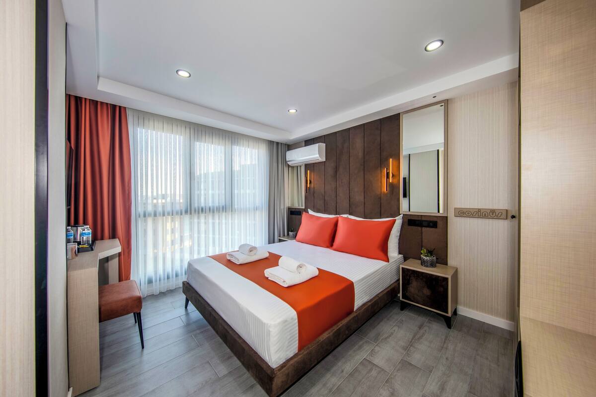 Quarto de hotel com uma cama grande, uma escrivaninha, uma cadeira, uma mesa de cabeceira e um espelho.