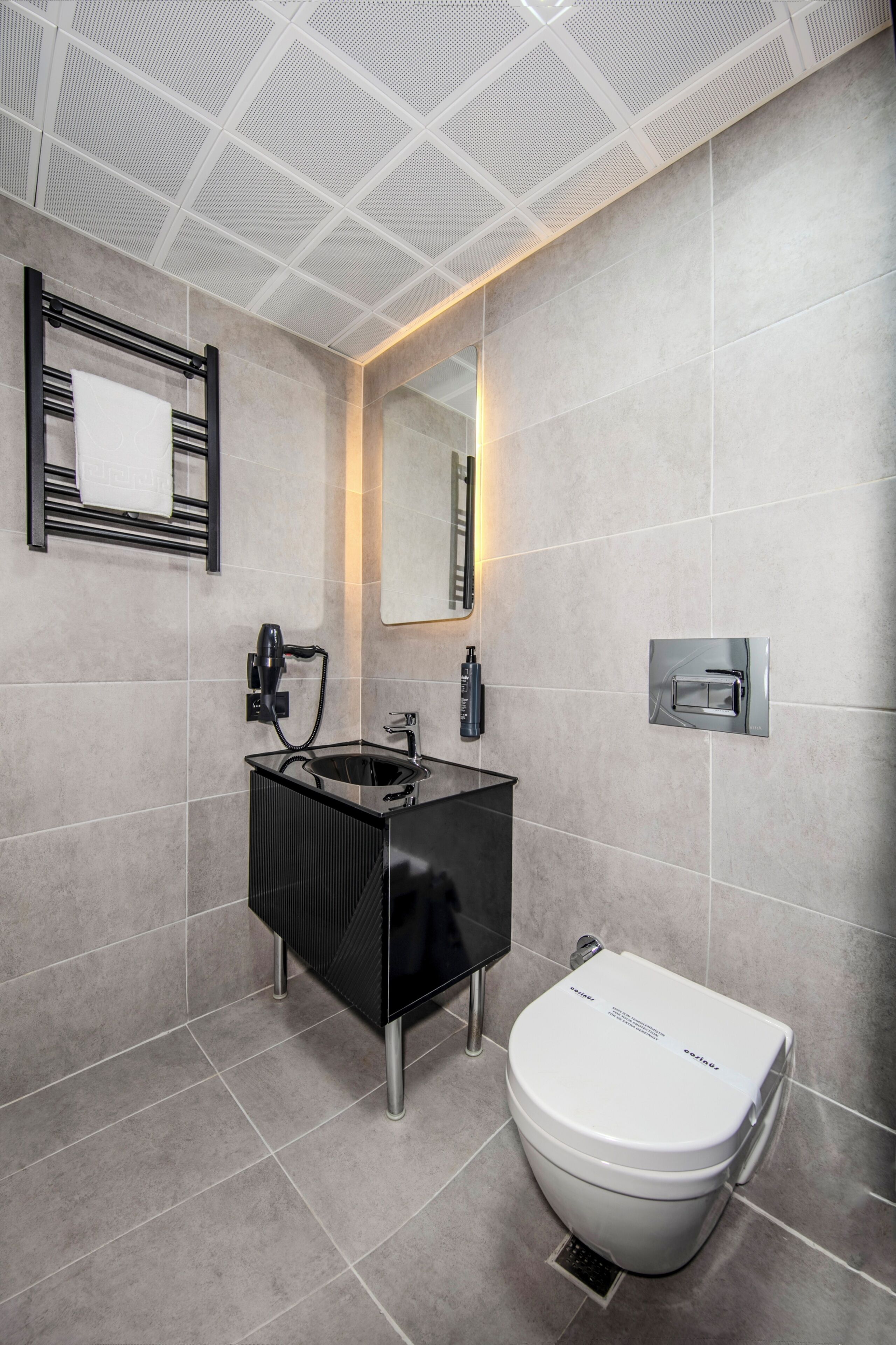 Un baño moderno con un tocador negro, un inodoro blanco e iluminación integrada en un espejo.
