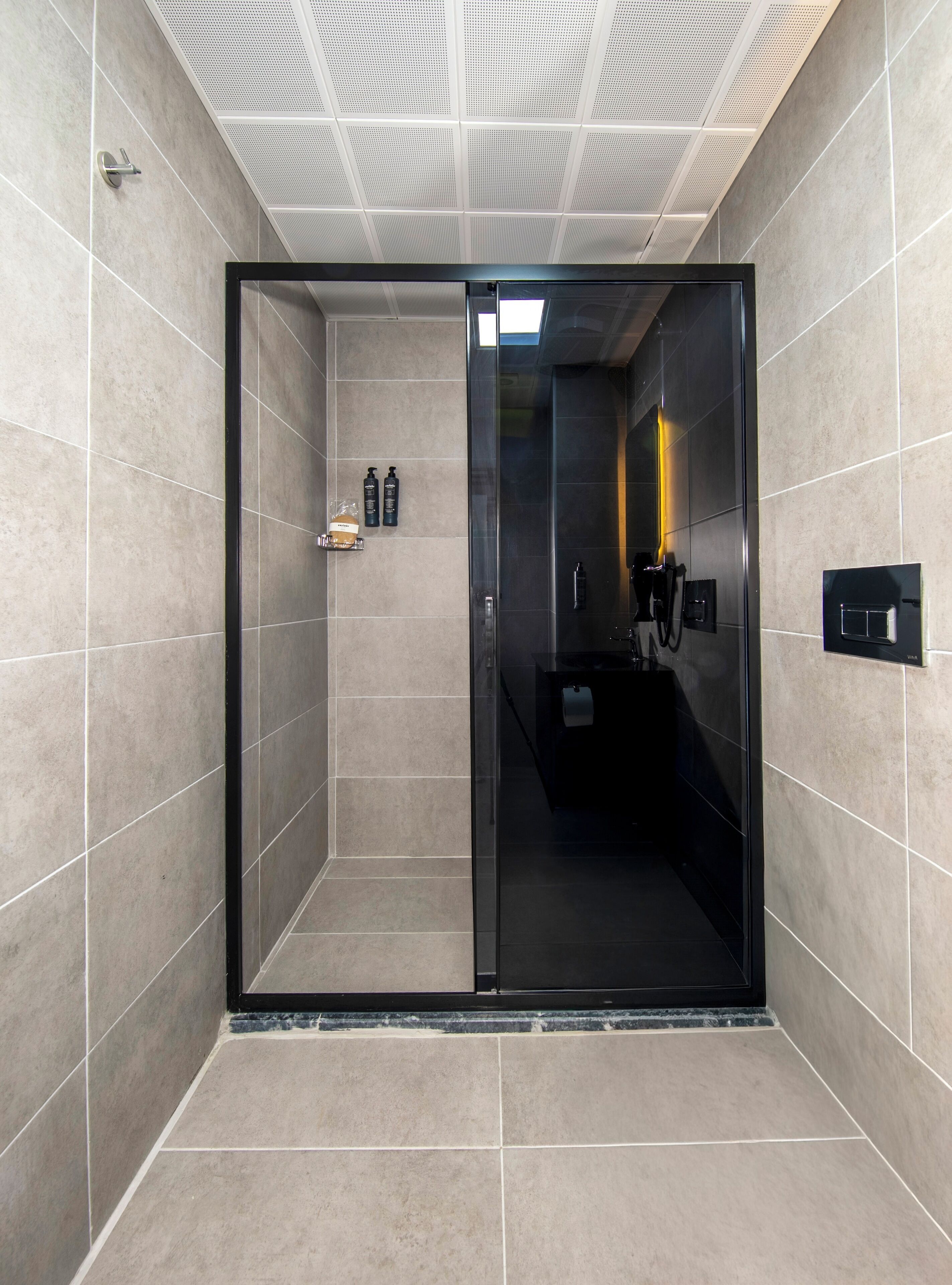 Un baño moderno con cabina de ducha de vidrio, un lavabo negro y un espejo.
