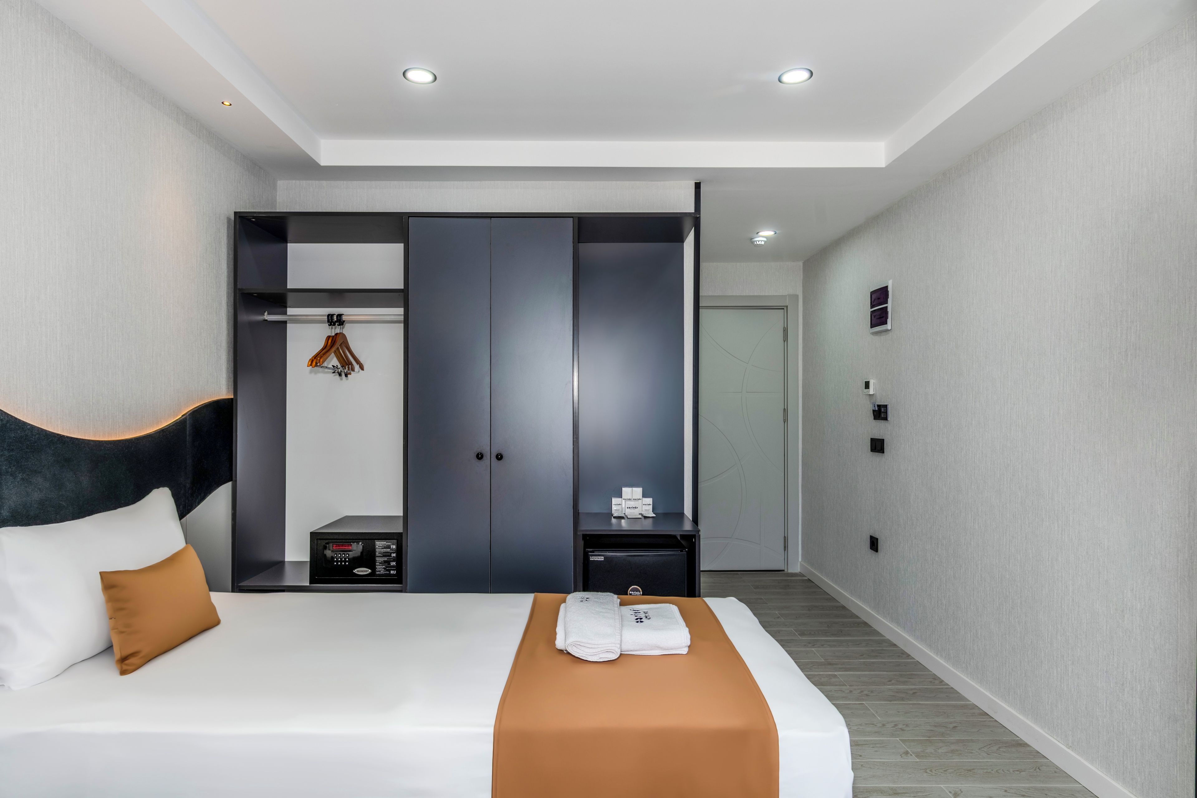 Habitación de hotel moderna con una cama grande, un armario, una mesita pequeña y la puerta del baño.