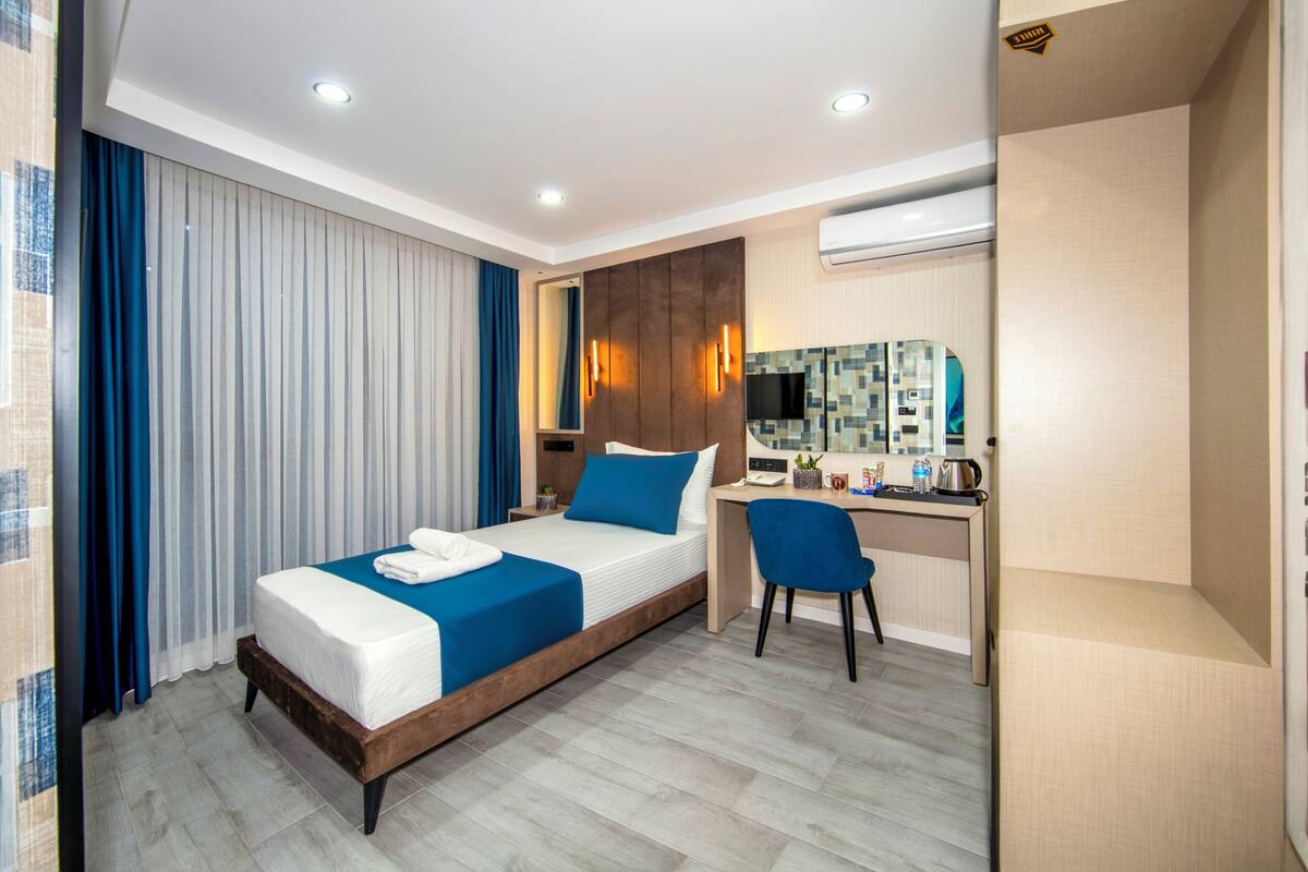 Quarto de hotel com cama, escrivaninha, cadeira e ar condicionado.