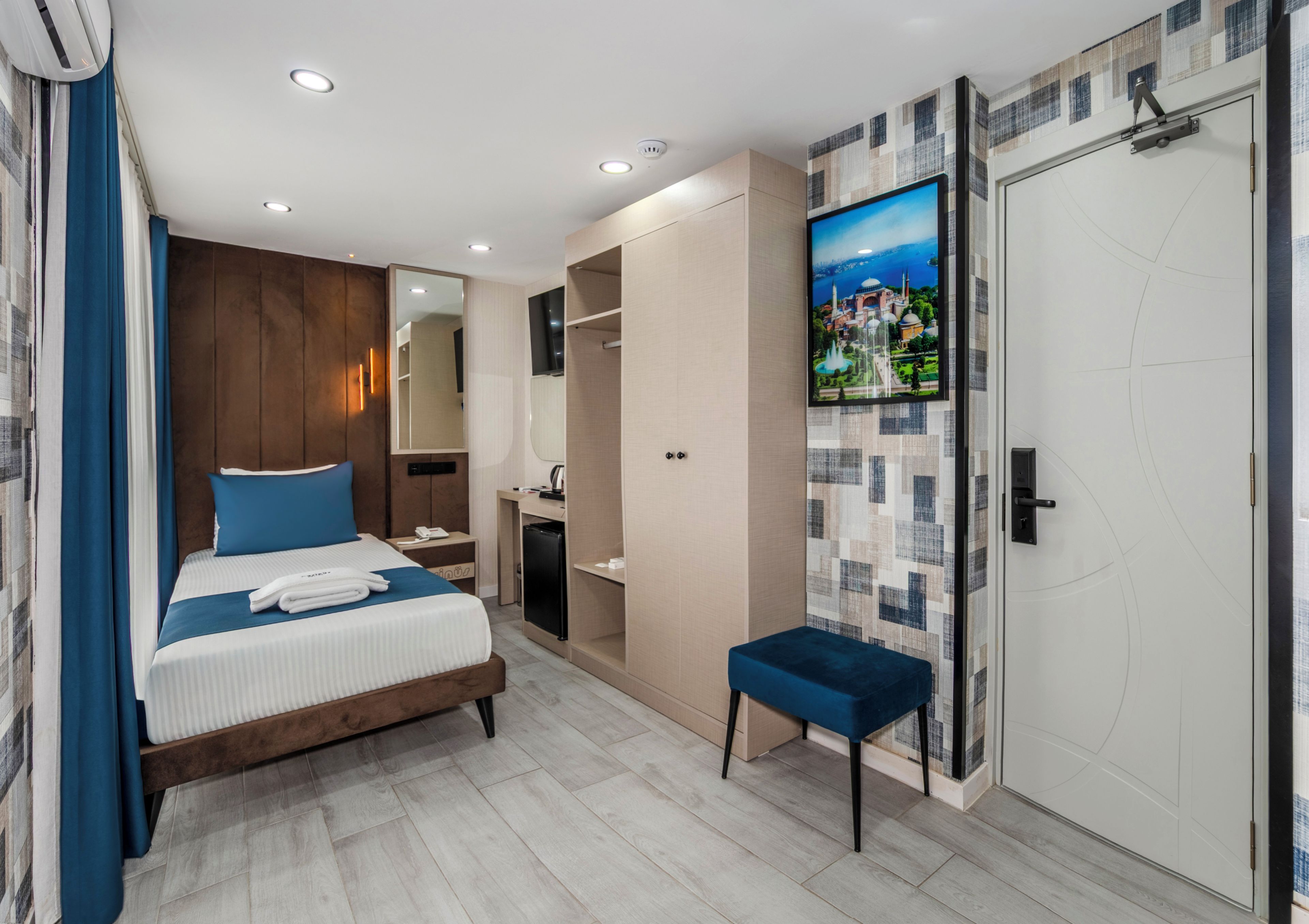 Una habitación de hotel moderna con cama, un banco, armario, espejo, televisor y zona de ducha.