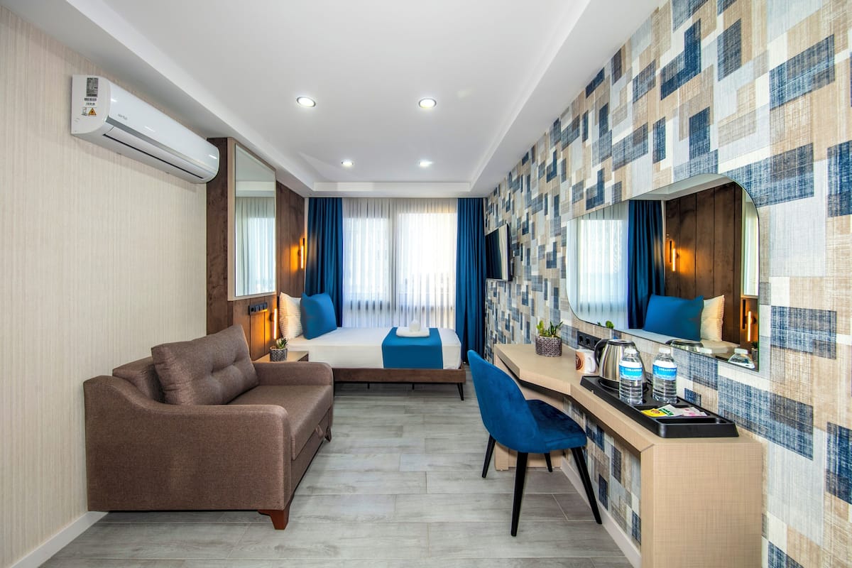 Quarto de hotel moderno com sofá, escrivaninha com espelho, cama com roupa de cama azul e parede estampada.