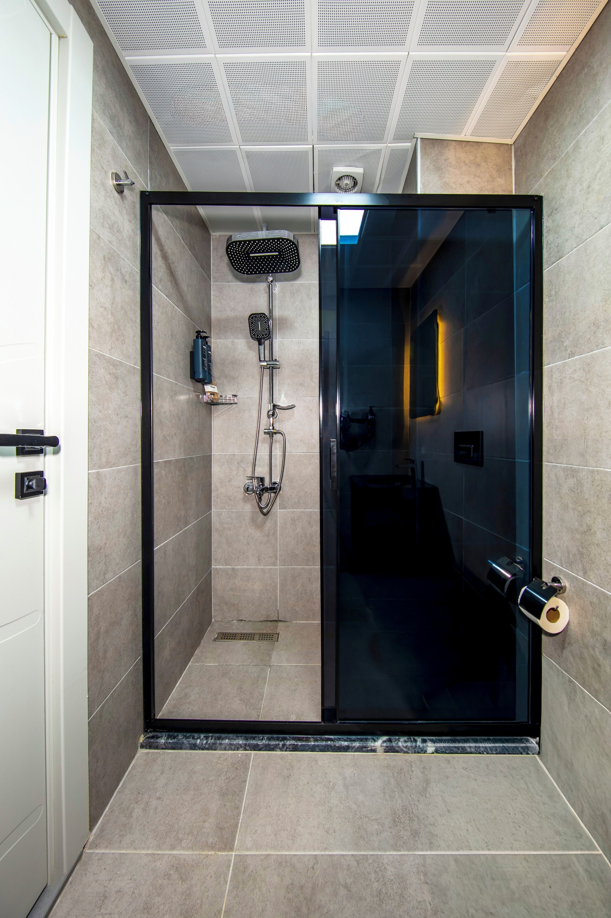 A modern shower area with a glass door, a handheld showerhead, and a wall-mounted fan.