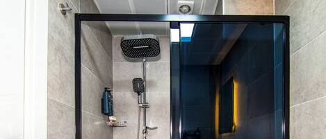 A modern shower area with a glass door, a handheld showerhead, and a wall-mounted fan.