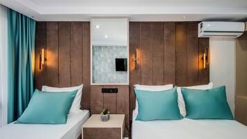 Ein Hotelzimmer mit zwei Betten, türkisfarbenen Kissen, einem kleinen Nachttisch mit Pflanze und einer Klimaanlage.