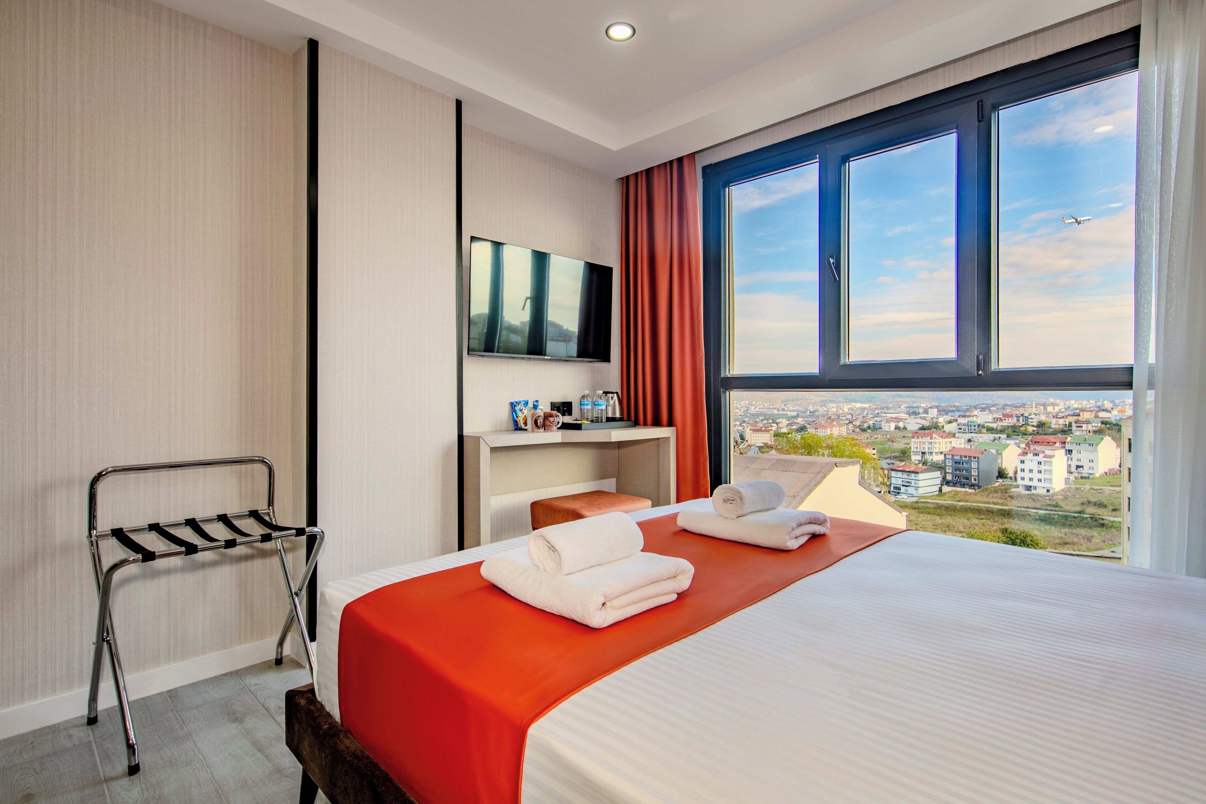 A hotel room with a bed, a TV, a desk, and a window with a city view.