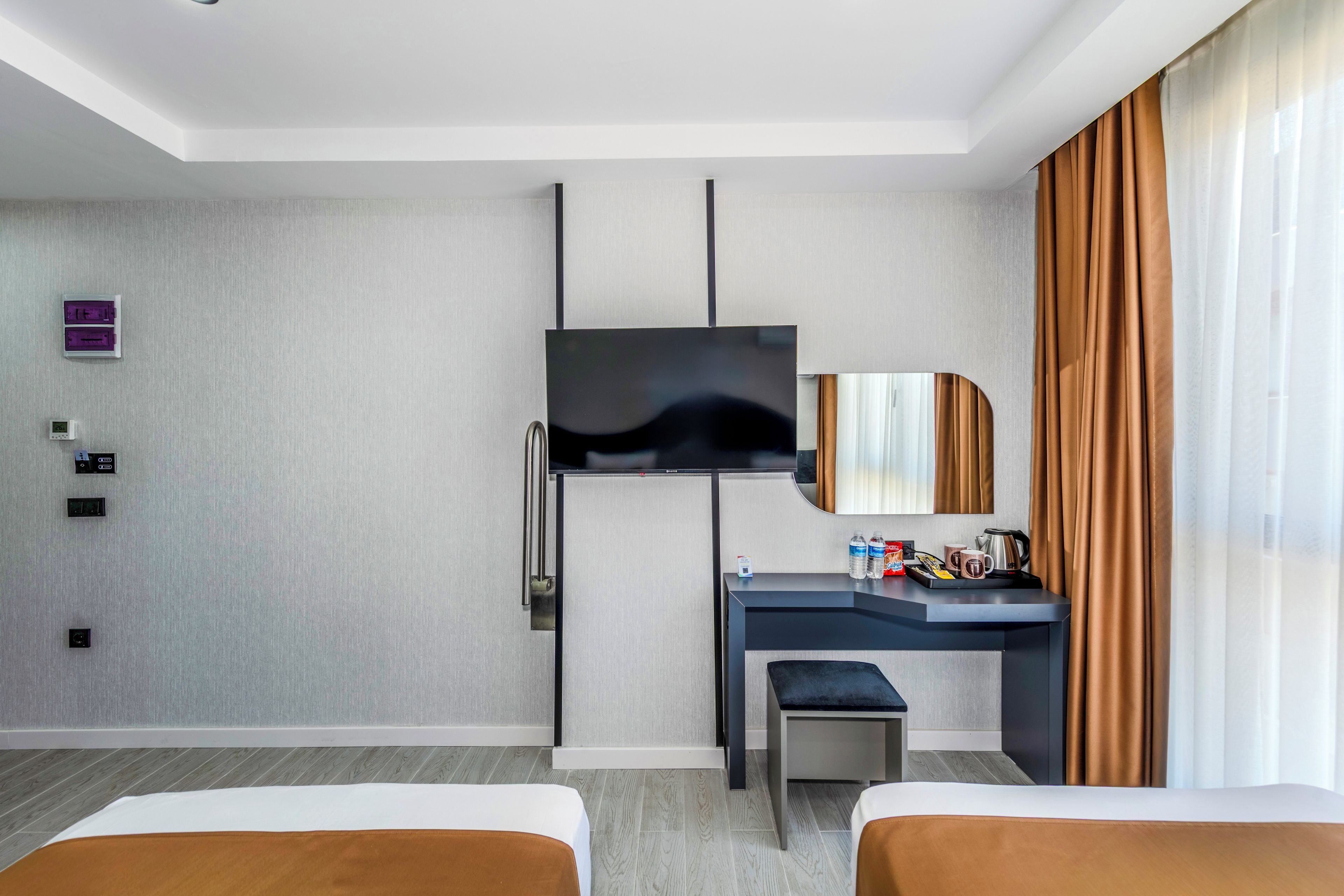 Habitación de hotel con cama, escritorio, televisión, espejo y ventana con cortinas.