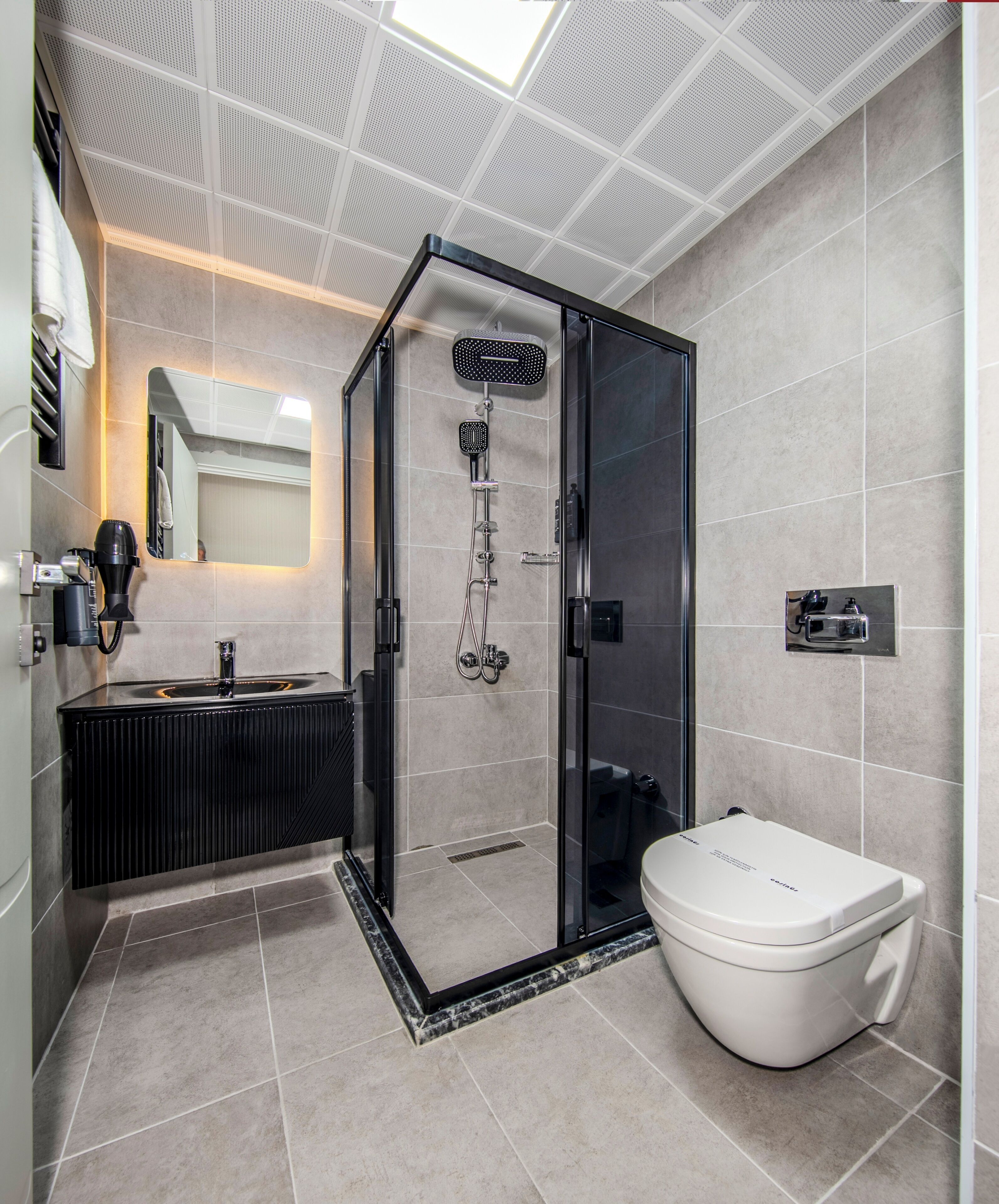 A modern bathroom with a glass-enclosed shower, a white toilet, and a black vanity with a hairdryer.