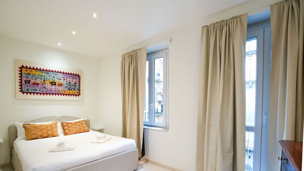 Une chambre à coucher avec un lit, des rideaux beiges, une fenêtre et une œuvre d’art colorée accrochée au mur.