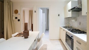 Une cuisine moderne avec des meubles blancs, une cuisinière à gaz et un four encastré. On y trouve un coin repas avec une table et des chaises blanches, ainsi qu'un vase posé sur la table.