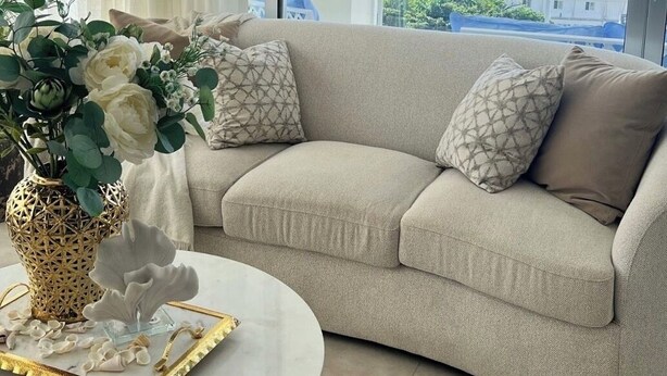 En stue med en beige sofa, en hvid vase med blomster og et rundt sofabord.