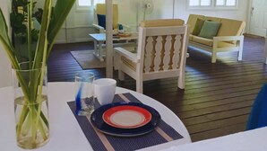 Un comedor con una mesa preparada para dos personas, un florero con plantas y un sofá al fondo.
