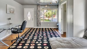 Una habitación con alfombra de estampado blanco y negro, un escritorio de vidrio con una silla, una puerta con un panel de vidrio decorativo y una ventana con cortinas.
