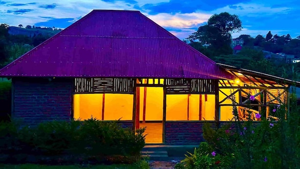 A rustic house with a sloped roof and a brick exterior, surrounded by greenery. - Lights of Kazinga Homestay (Kichwamba)