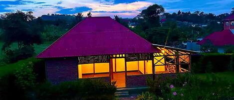 Una casa con techo rojo y un interior bien iluminado, rodeada de follaje y un cielo despejado.