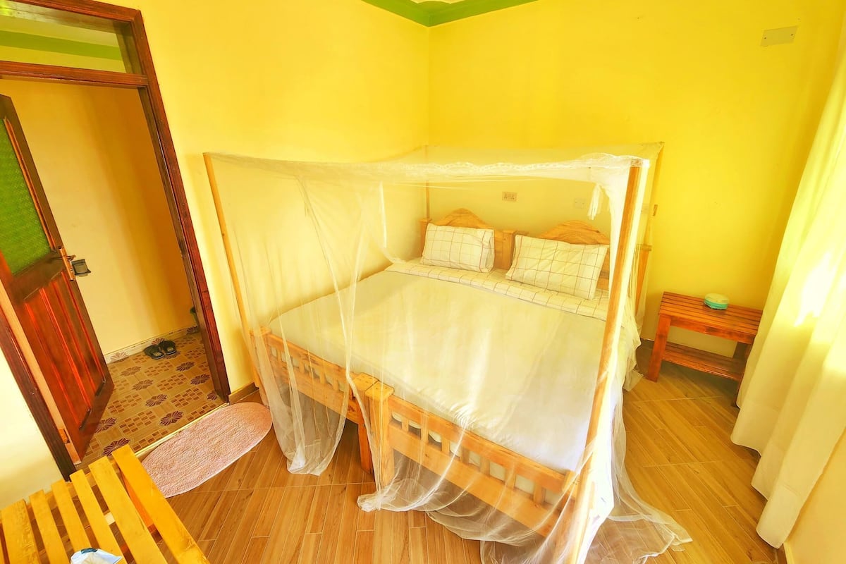 A room with a bed under a mosquito net, a wooden bench, and a small table with a green object on it.