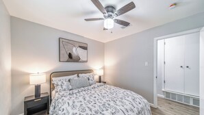 A bedroom with a bed, two bedside tables with lamps, a ceiling fan, a door, and a wall-mounted artwork. - 3-bed house in Denton, pool, games, firepit in a huge private fenced yard (Denton)
