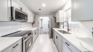 A modern kitchen with stainless steel appliances, white cabinetry, and a large window. - 3-bed house in Denton, pool, games, firepit in a huge private fenced yard (Denton)