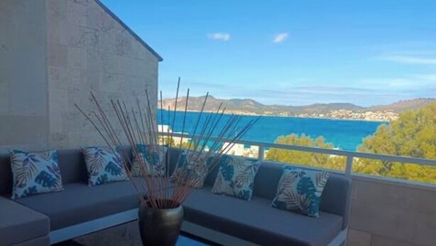Een balkon met een bank en een tafel, met uitzicht op een wateroppervlak en heuvels in de verte.