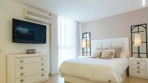 Een slaapkamer met een bed, een televisie aan de muur, een nachtkastje met een lamp en een kledingkast.