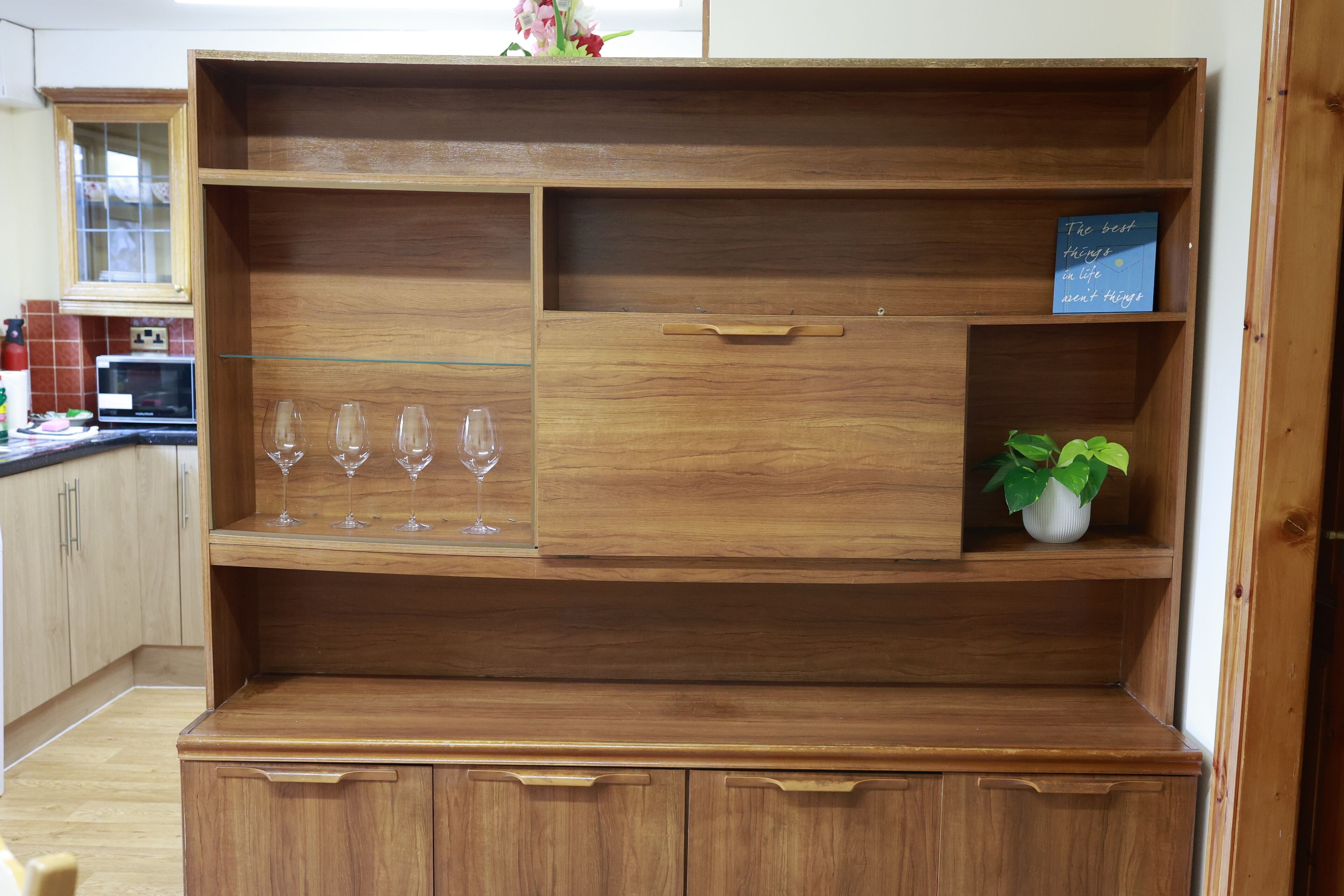Un meuble en bois doté de plusieurs compartiments, dont une section pour les verres à vin et un petit pot de plante.