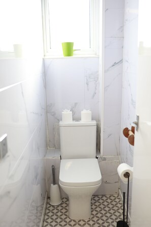 Um banheiro pequeno com vaso sanitário, uma xícara verde no parapeito da janela e ladrilhos de chão estampados.