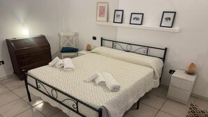A neatly made bed with rolled towels, a wooden dresser, a nightstand with a salt lamp, and a wall with framed pictures. - Comfort in the heart of Bari (Bari)