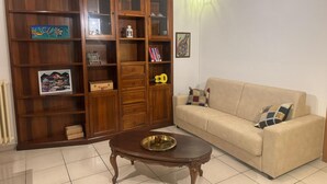 A living room with a wooden cabinet, a beige sofa, a coffee table, and a wall-mounted light fixture. - Comfort in the heart of Bari (Bari)