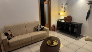 A living room with a beige sofa, a wooden coffee table, a black side table with a guitar, and a wall-mounted lamp. - Comfort in the heart of Bari (Bari)
