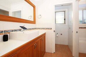 A bathroom with a white sink, wooden cabinets, a mirror, and a tiled backsplash. - Coolaroo Beach House - Rural Bliss by the Coast (Berry)