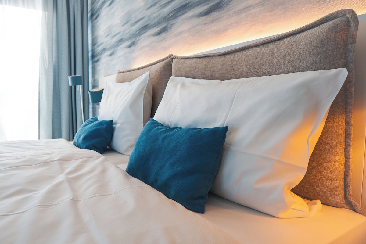 A neatly made bed with white and teal pillows, a wooden headboard, and a modern headboard design.