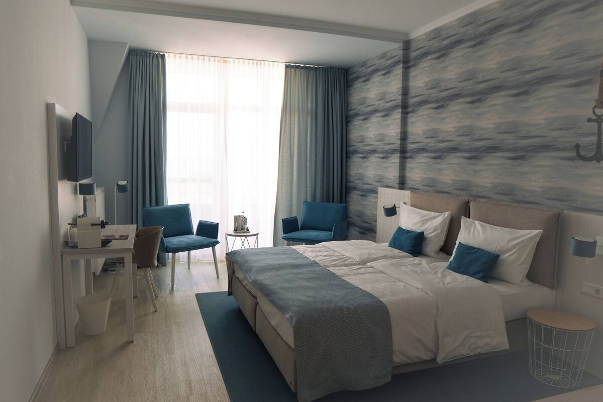 A modern hotel room with a large bed, two chairs, a desk, and a TV.