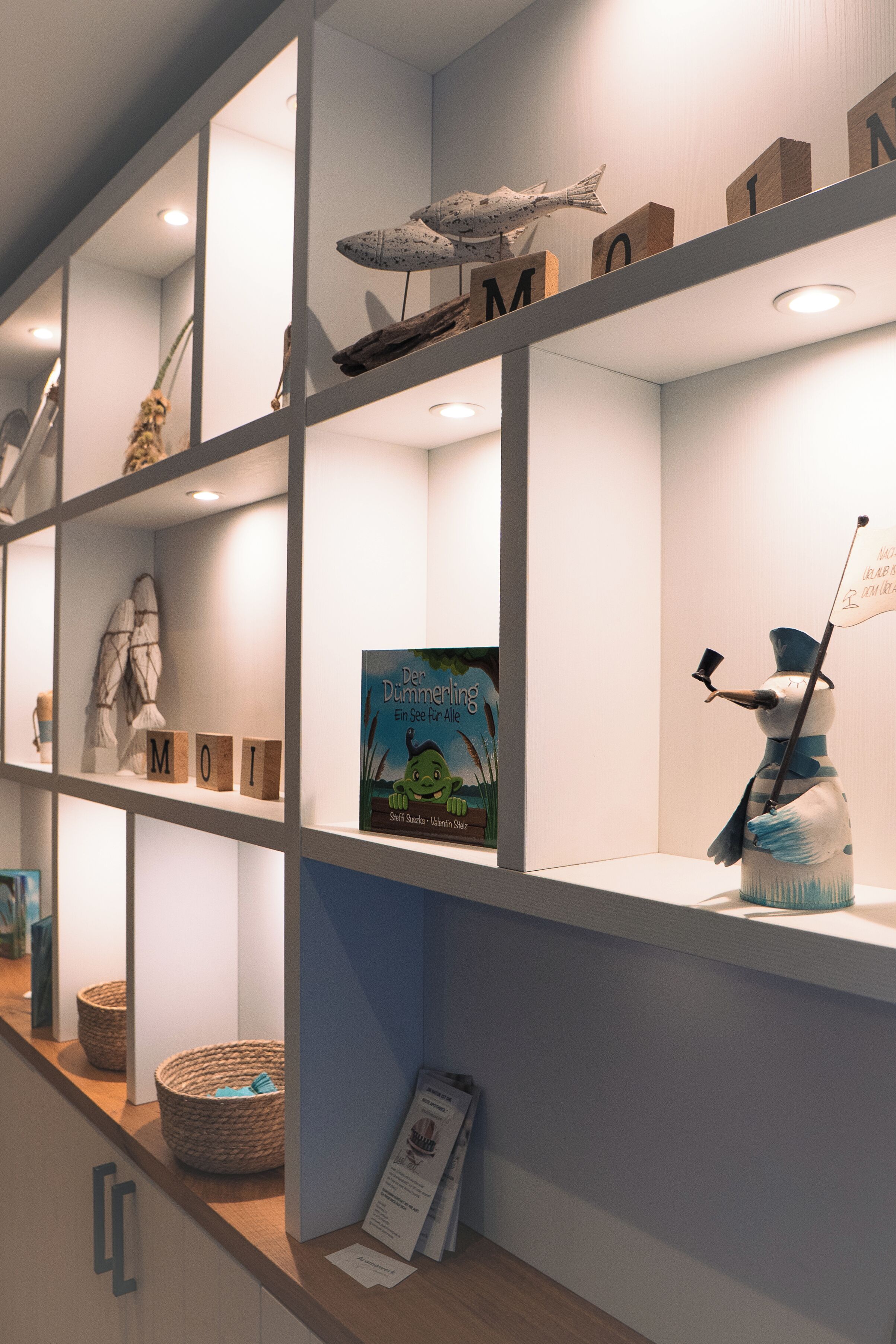 Una presentación bien iluminada con bloques de madera que deletrean "MOM", un libro titulado "Der Dummeling" y una figurita decorativa de muñeco de nieve.