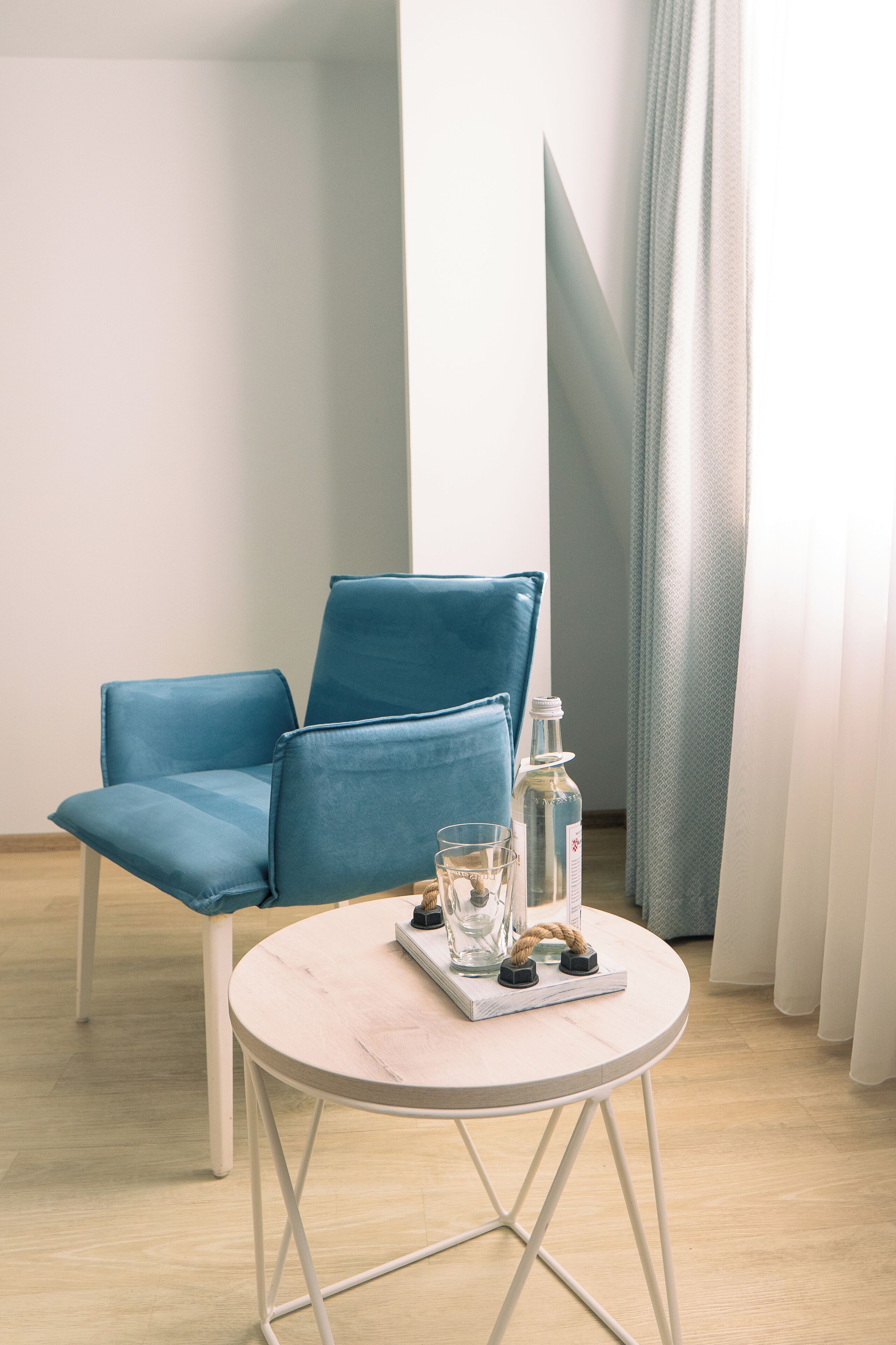 A room with a blue chair, a round table with a tray, a bottle, and glasses.
