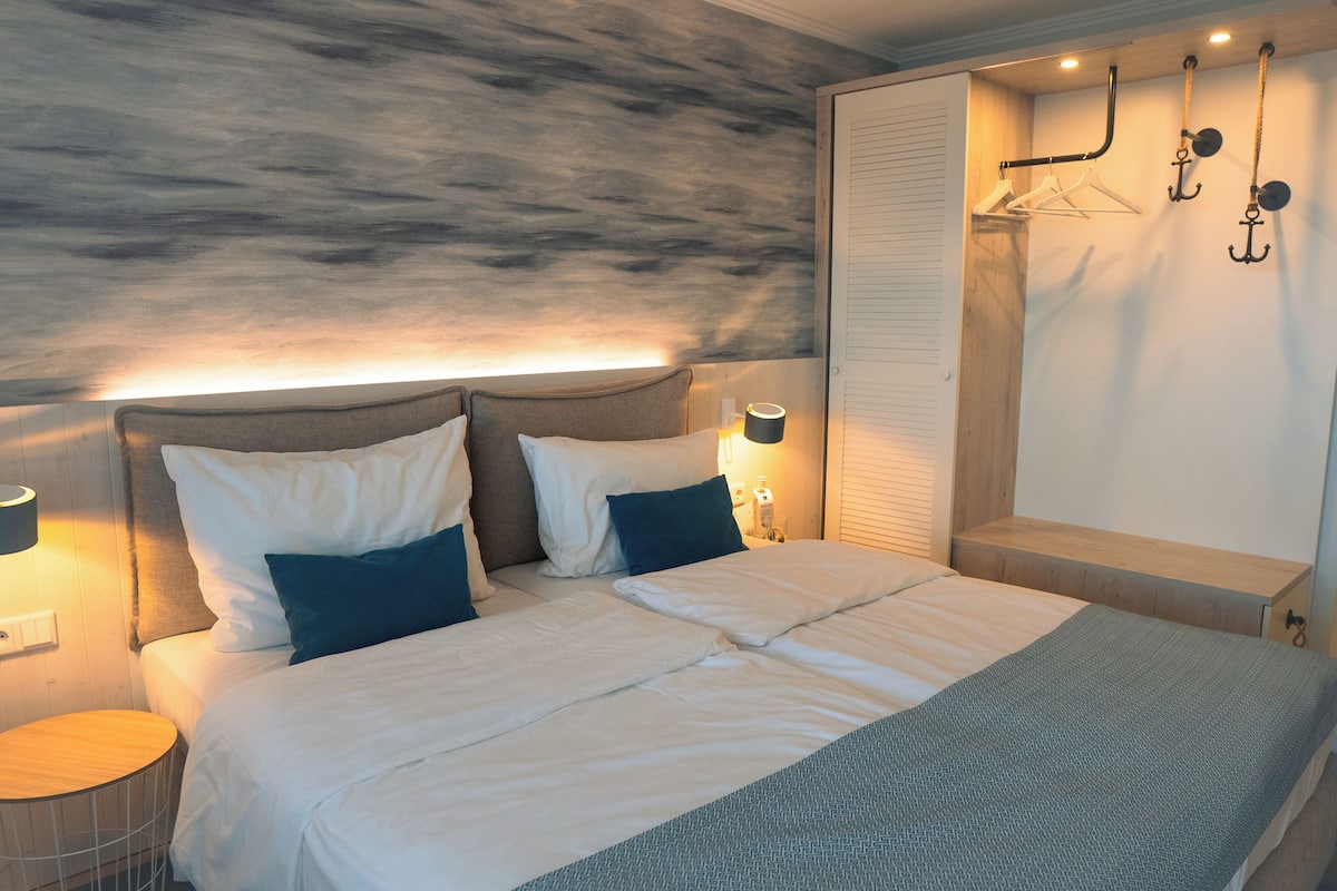 A neatly made bed with white and blue bedding, a headboard, bedside lamps, and a wooden bench.