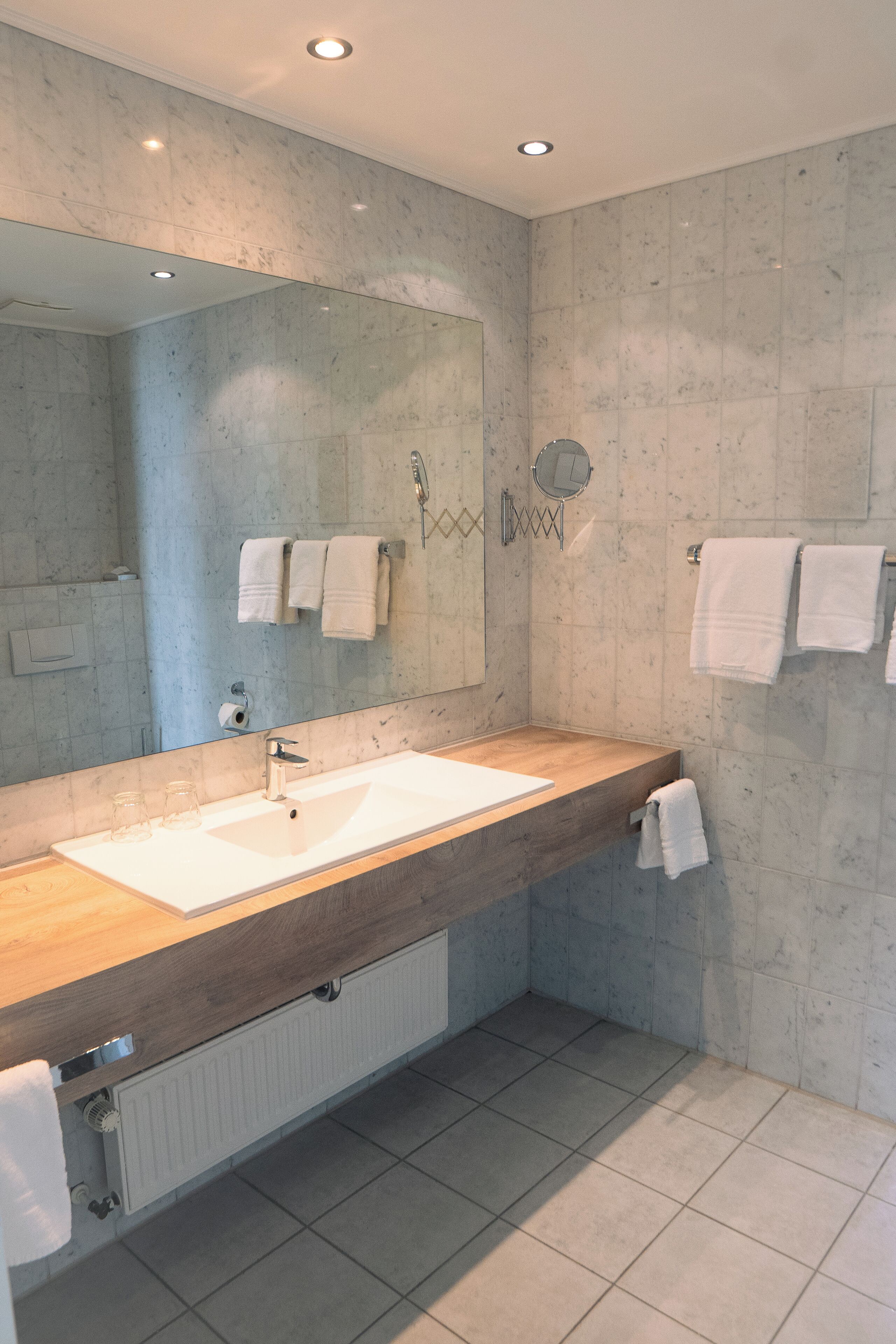 A modern bathroom with a large mirror, two sinks, and a wooden vanity.