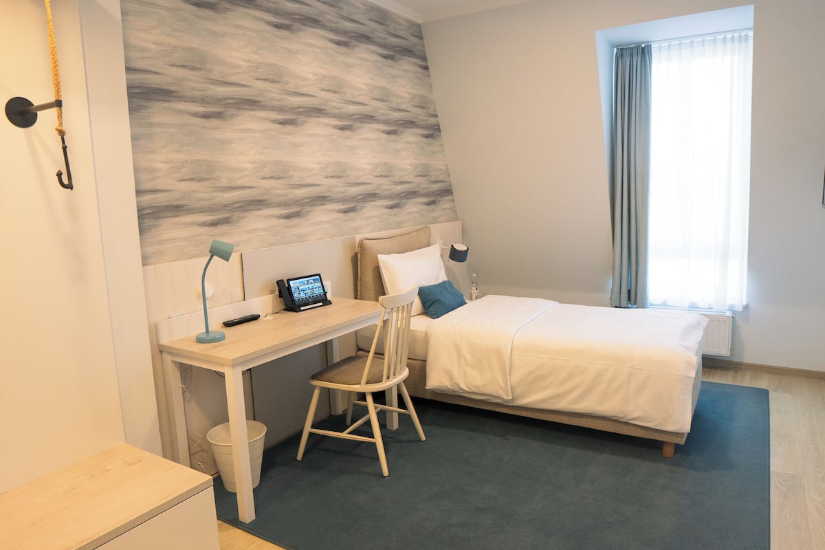 A bedroom with a bed, a desk with a chair, a computer, and a window with curtains.