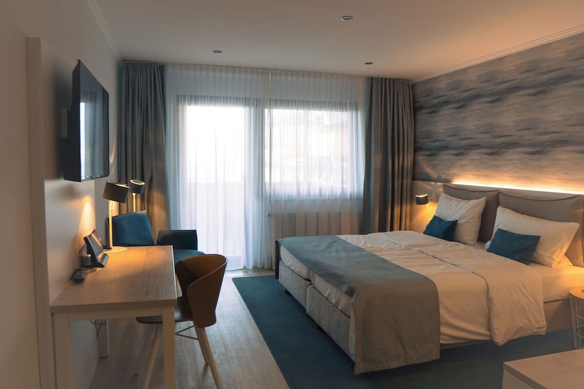A hotel room with a bed, bedside table, lamp, chair, and a TV mounted on the wall.