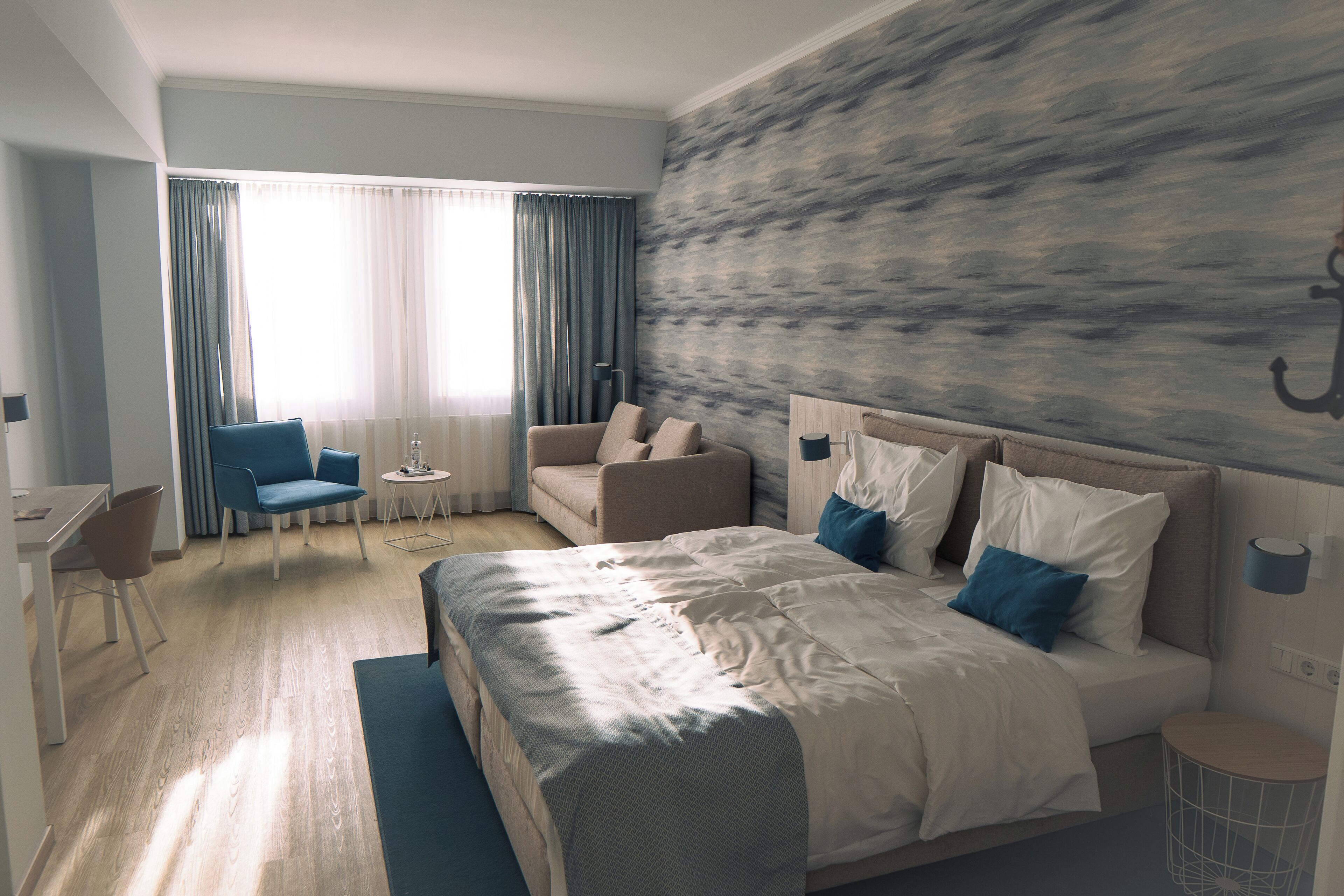 Habitación de hotel moderna con una cama grande, dos zonas de estar, una mesita y vistas al exterior.