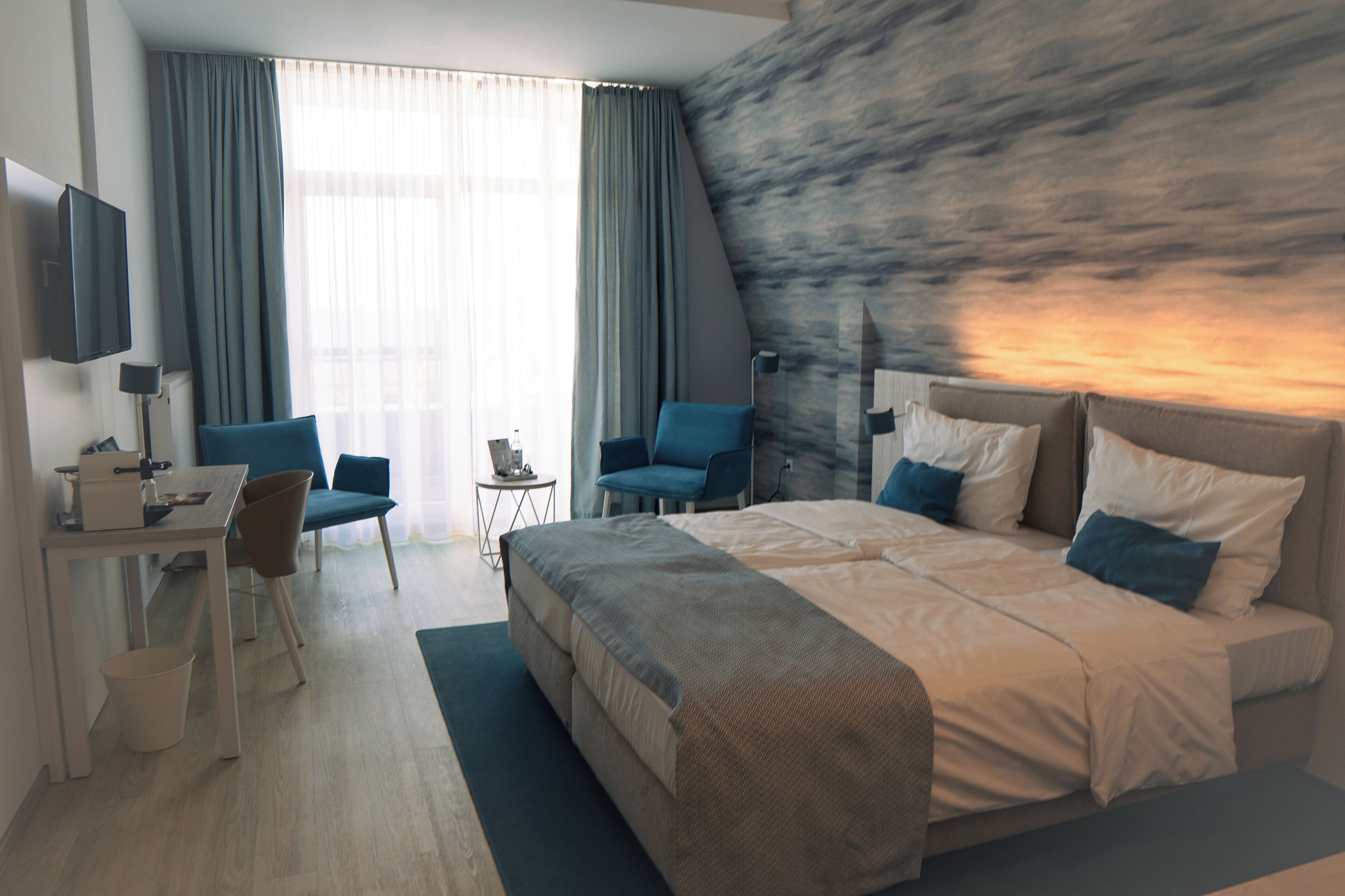 Una habitación de hotel moderna con una cama grande, dos sillones, un escritorio con ordenador y un televisor.