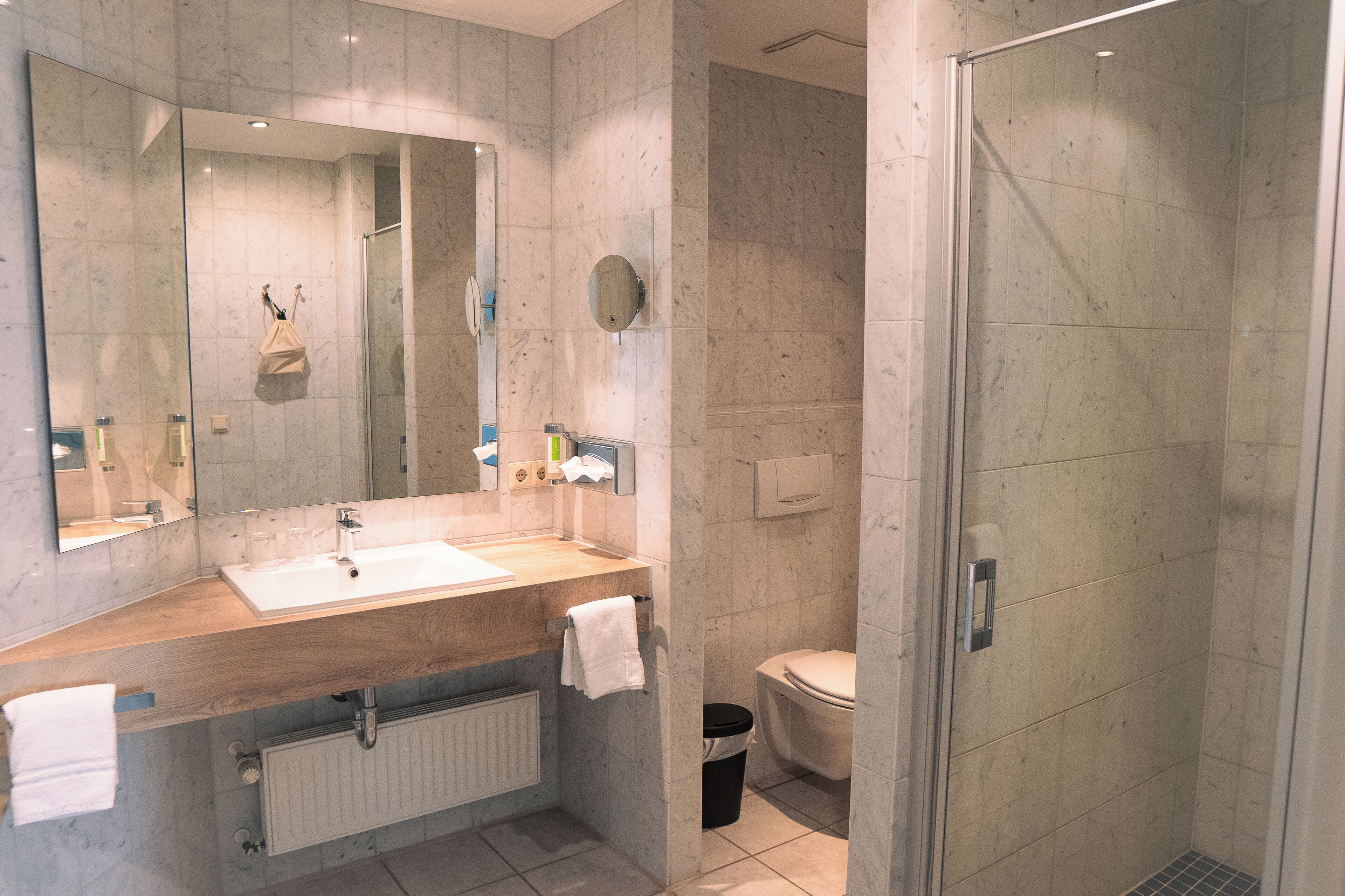 Een moderne badkamer met een houten wastafelmeubel, een grote spiegel, een toilet en een douchecabine van glas.